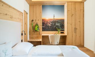 A modern room with wooden paneling and a cozy bed. On the wall hangs a picture of a sunrise over a mountain landscape.