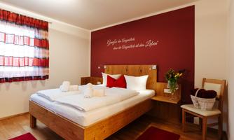 A cozy bedroom with a large bed, red pillows, and modern wooden furniture. On the wall, there is an inspiring quote, and the room is designed to be bright and welcoming.