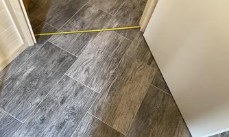 A modern floor made of gray tiles can be seen. A measuring tape is on the ground, and a door is visible in the background.