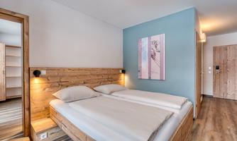 A modern bedroom with a double bed and wooden elements. The walls are painted in soft colors, and a picture hangs on the wall.