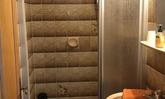 A small bathroom with a shower enclosure and a sink. The walls are decorated with brown tiles.