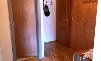 A bright hallway with wood paneling and laminate flooring. Coat hooks hang on the wall and a door leads to another room.