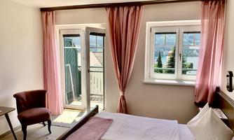 A bright bedroom with a double bed and a cozy chair. Large windows offer a view of nature.