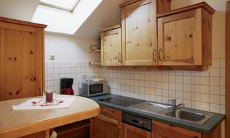 A cozy kitchen with wooden cabinets and a large window. On the counter, there is a mug and a small decoration.