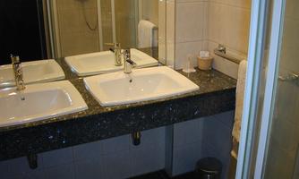 A modern bathroom with two sinks and an elegant sink cabinet. The walls are brightly tiled, and there is a shower cabin.