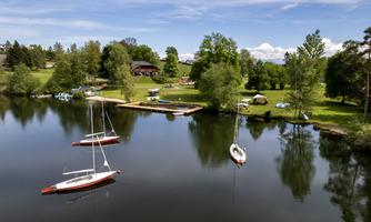 A tranquil landscape with a lake and sailboats. Surrounded by green trees and a blue sky.
