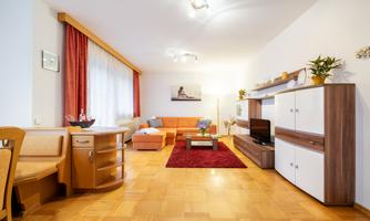 A cozy living room with furniture in warm colors. A red carpet and large windows create an inviting atmosphere.