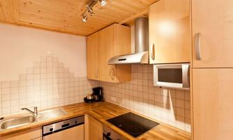 A modern kitchen with wooden cabinets and bright tiles. It is equipped with a stove, a sink, and a microwave oven.