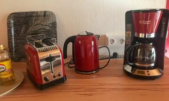 A modern kitchen corner with a red toaster, a kettle, and a coffee machine. Everything is on a wooden countertop.