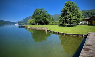 A tranquil lake with clear water and green meadows. In the background, there are trees and gentle hills.