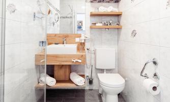 A modern bathroom with a clear glass shower and a wooden vanity. Towels are neatly stacked on a shelf.