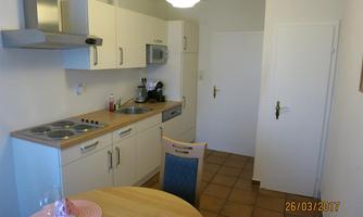 A modern kitchen with wooden surfaces and white cabinets. A dining table with seats for two people is also visible.