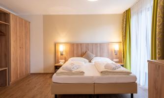 A cozy bedroom with a double bed and hardwood flooring. Large windows let in plenty of light, and the walls are painted in soft hues.
