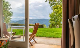 Large terrace door with a view of the meadow, mountains, and seating area in front of the house. Children can play directly in front of the apartment while adults sit on the terrace and enjoy the view.