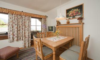 A cozy dining area with a wooden table and chairs. The windows are adorned with colorful curtains and there is a small television.