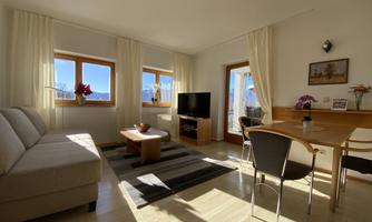 A bright living room with large windows and a view. There is a sofa, a table, and a television.