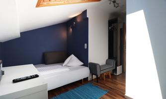 A modern room with a single bed and a seating area. The walls are painted blue, and the floor is made of wood.