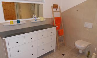 A modern bathroom with a white vanity and a dark countertop. There is a large mirror wall and an orange towel ladder.
