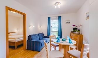 A cozy room with a sleeping area and a sitting area. A round table set with plates and chairs, as well as a sofa, can also be seen.