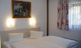 A cozy bedroom with a double bed and two pillows. A painting hangs on the wall, and the windows have curtains with floral patterns.