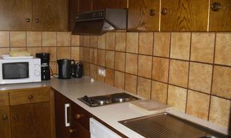 A spacious kitchen with wooden cabinets and a countertop made of white material. The amenities include a microwave, a coffee maker, and a dishwasher.