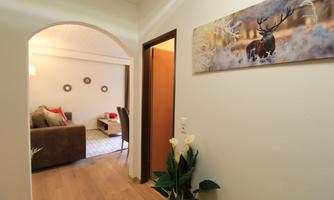 A bright hallway with a cozy living room in the distance. On the wall hangs a picture of a deer in a wintry landscape.