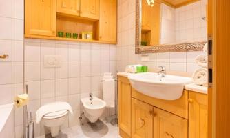 A modern bathroom with wooden elements and a large mirror. It contains a shower, a sink, and fresh towels.