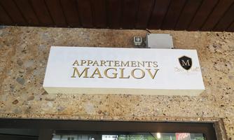 A sign with the inscription "Appartements Maglov" in golden letters. It hangs on a wall made of light stone.