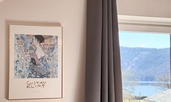 A modern room with a window that offers a view of a lake. A painting by Gustav Klimt hangs on the wall.