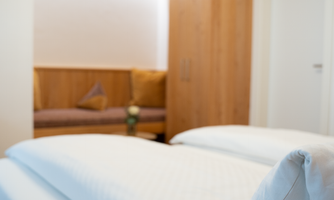 A bright and inviting bedroom with two beds. In the background, there is a cozy wooden seating area.