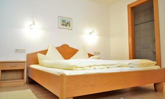 A simple bedroom with a wooden bed and white bed covers. On the wall, there are two bedside lamps and a small picture.