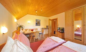 A cozy bedroom with wooden paneling and a double bed. There is a table with chairs and a wardrobe.