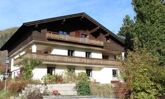 A traditional old house with a wooden balcony and white walls. Surrounded by a beautiful garden landscape and trees.