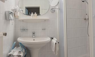A modern bathroom with a sink, a mirror, and a shower cubicle. The walls are tiled and a fabric laundry basket is in the corner.
