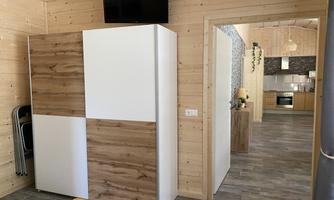 A modern room with a wooden shelf and a TV on the wall. In the background, a open kitchenette can be seen.