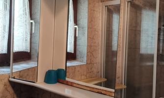 A bathroom with a large mirror cabinet and two windowless walls. On the shelf are two blue objects.