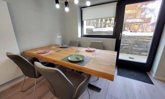 A modern dining area with a large wooden table and elegant chairs. A lot of light streams through the window, and the table decoration is colorful.