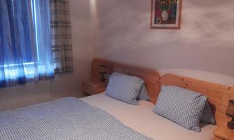 A cozy bedroom with a double bed and checkered bedding. A picture of sunflowers hangs on the wall.