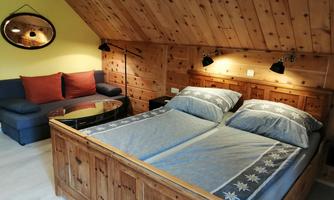 Room with wooden bed and separate duvets under a sloped ceiling, wood paneling on wall and ceiling, blue sofa with table and wall mirror.