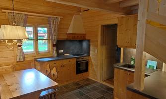 A cozy wooden kitchen with a dining table, a stove, and a sink. Windows let in plenty of light and create a pleasant atmosphere.
