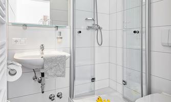 A modern bathroom with a shower, a sink, and a toilet. On the shower floor, there is a yellow rubber duck.