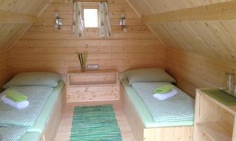 A cozy room with wood paneling and two single beds. There is a small table, a green carpet, and some decorative elements.
