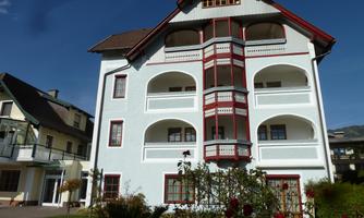 A cozy, multi-story building with white walls and red accents. Surrounded by a well-maintained garden landscape.