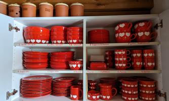A kitchen cabinet with red-colored dishes adorned with white hearts. The glasses, cups, and plates are neatly organized.