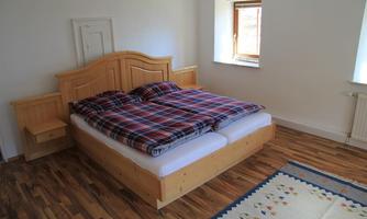 A cozy bedroom with a wooden bed and checked bedspreads. The room has light walls and a carpet on the floor.