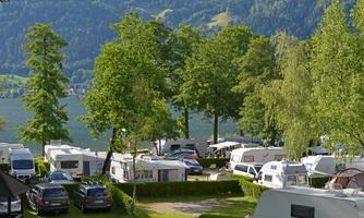 A campsite surrounded by trees and mountains. Several RVs and cars are parked in the green surroundings.