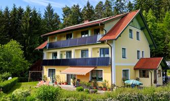 A charming multi-family house with solar panels and colorful flowers in the garden. The surrounding nature and trees provide a tranquil atmosphere.
