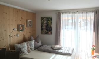 A cozy living room with wood paneling and large windows. There is a sofa and a table decorated with flowers.