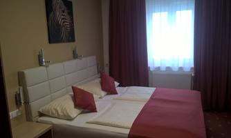 A comfortable hotel room with a double bed and red pillows. The room has bright curtains and modern wall decor.