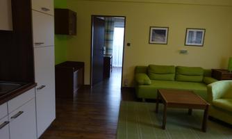 A modern living room with a green couch and a wooden table. The walls are painted in soft colors and there are pictures on the walls.